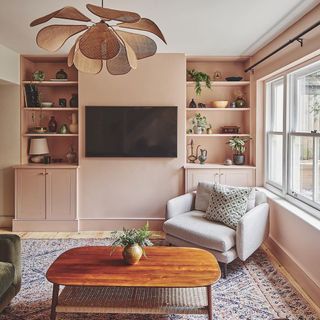 Relaxed blush lounge with wall mounted TV, rattan feature pendant, boho rug, recessed shelving alcoves with plants, and retro inspired furniture.