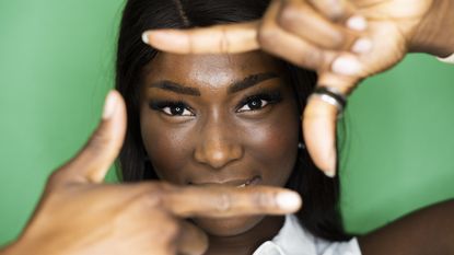 A woman holds her fingers up in front of her face like she&#039;s framing a photo.