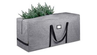 A gray fabric Christmas tree storage bag with black handles and a tree branch sticking out on top, for the best Christmas tree storage bags.