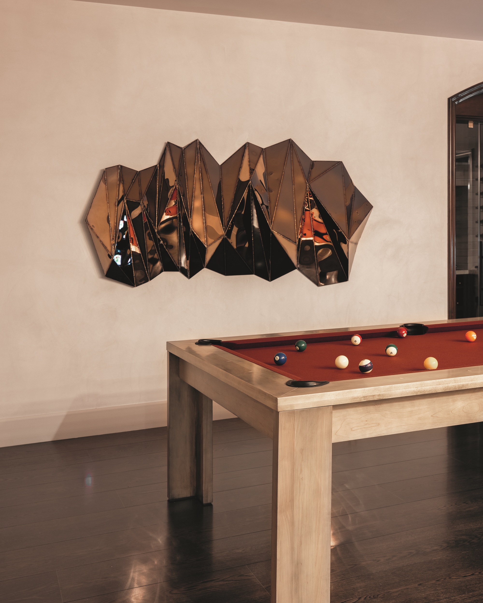 games room with large metallic sculpture on the wall, light timber and red pool table, dark timber floorboards, and plaster walls