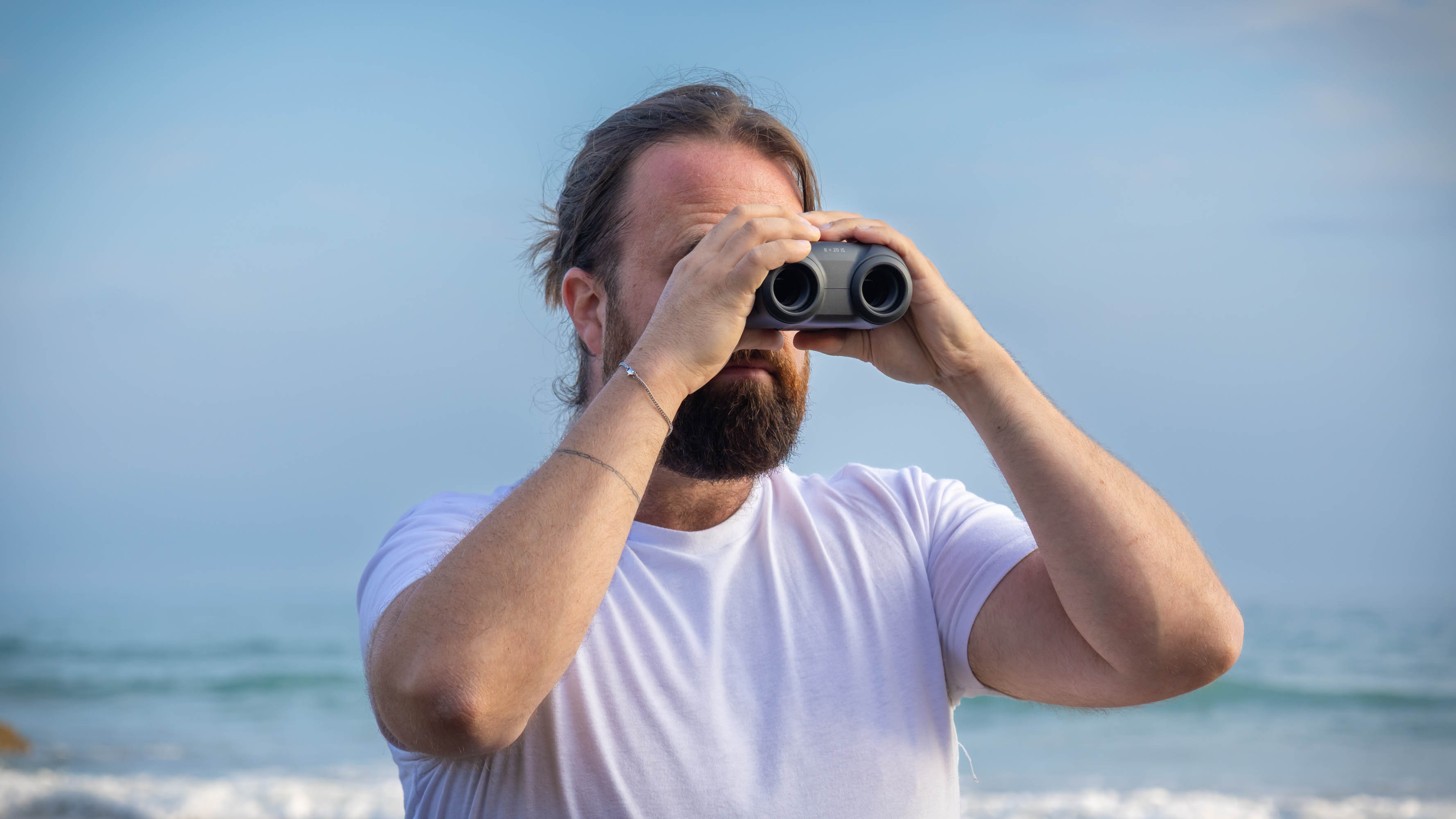 A male using the Canon 8x20 IS binoculars with the sea behind them.