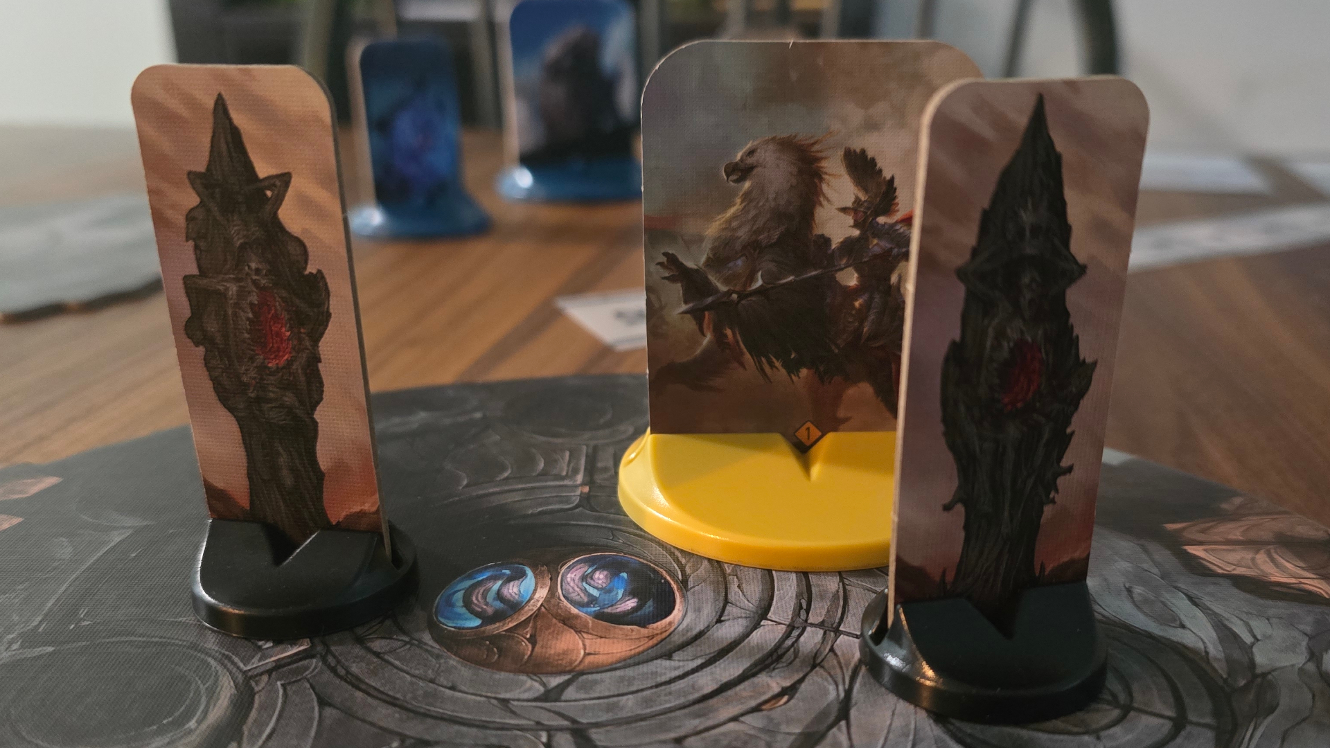 Malediction cardboard standees on terrain tokens, placed on a wooden table