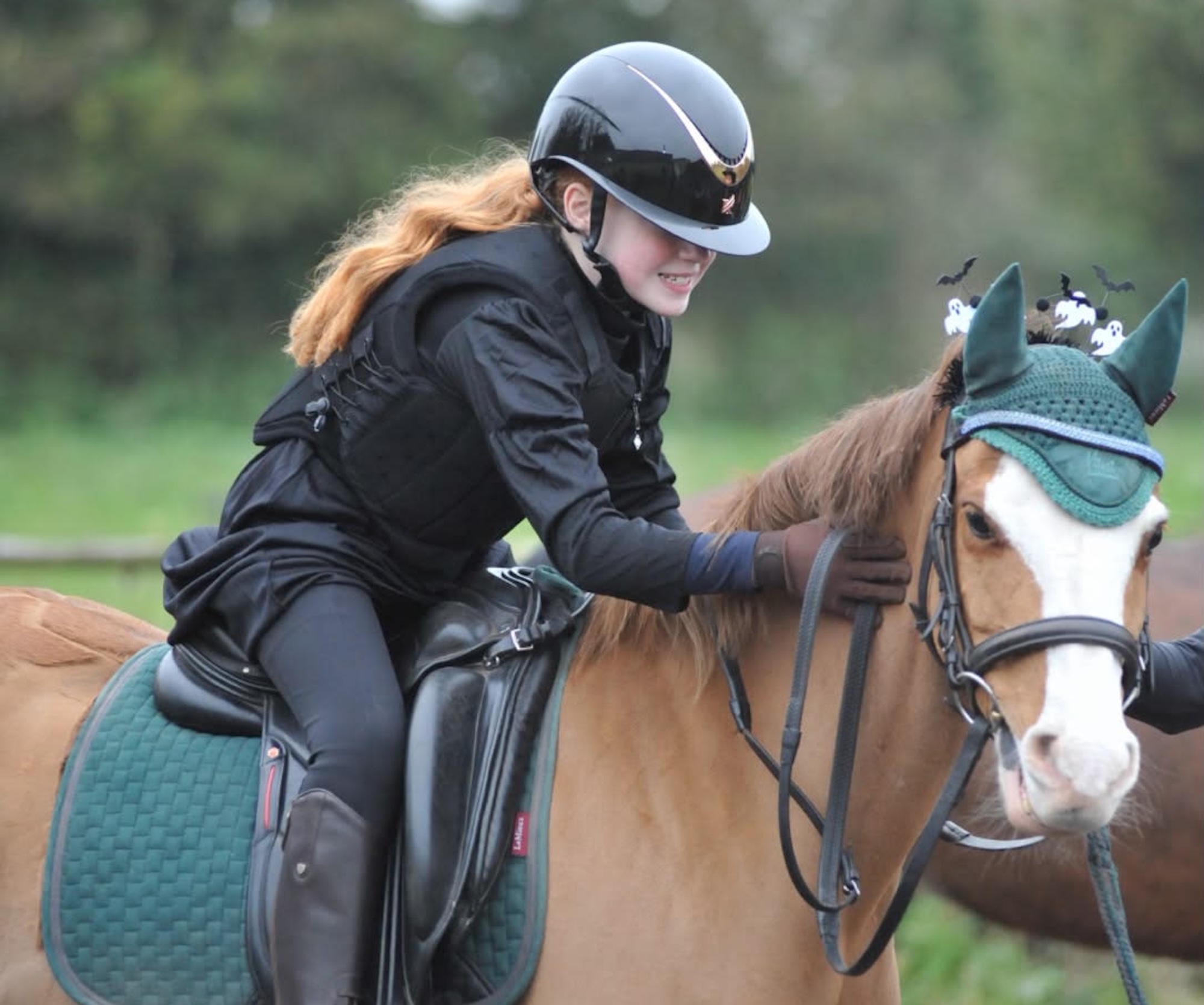 A young girl riding and patting a chestnut pony