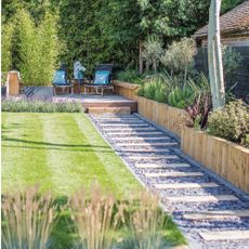 A garden with a tidy lawn and flowerbeds, wooden deck, raised bed edging, and plank path, and grey fence and sun loungers