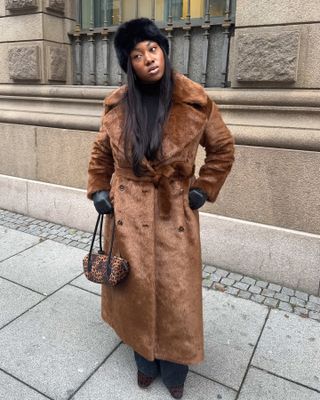 Woman in faux-fur hat, coat, and leopard print bag.