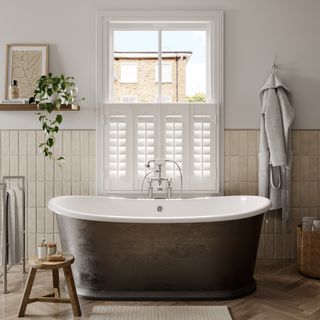 coastal bathroom with white shutters, cream wall tiles, wood effect floor, shelf, artwork, stool, freestanding bath