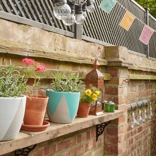 designed plant pots on wooden shelf of red brick wall