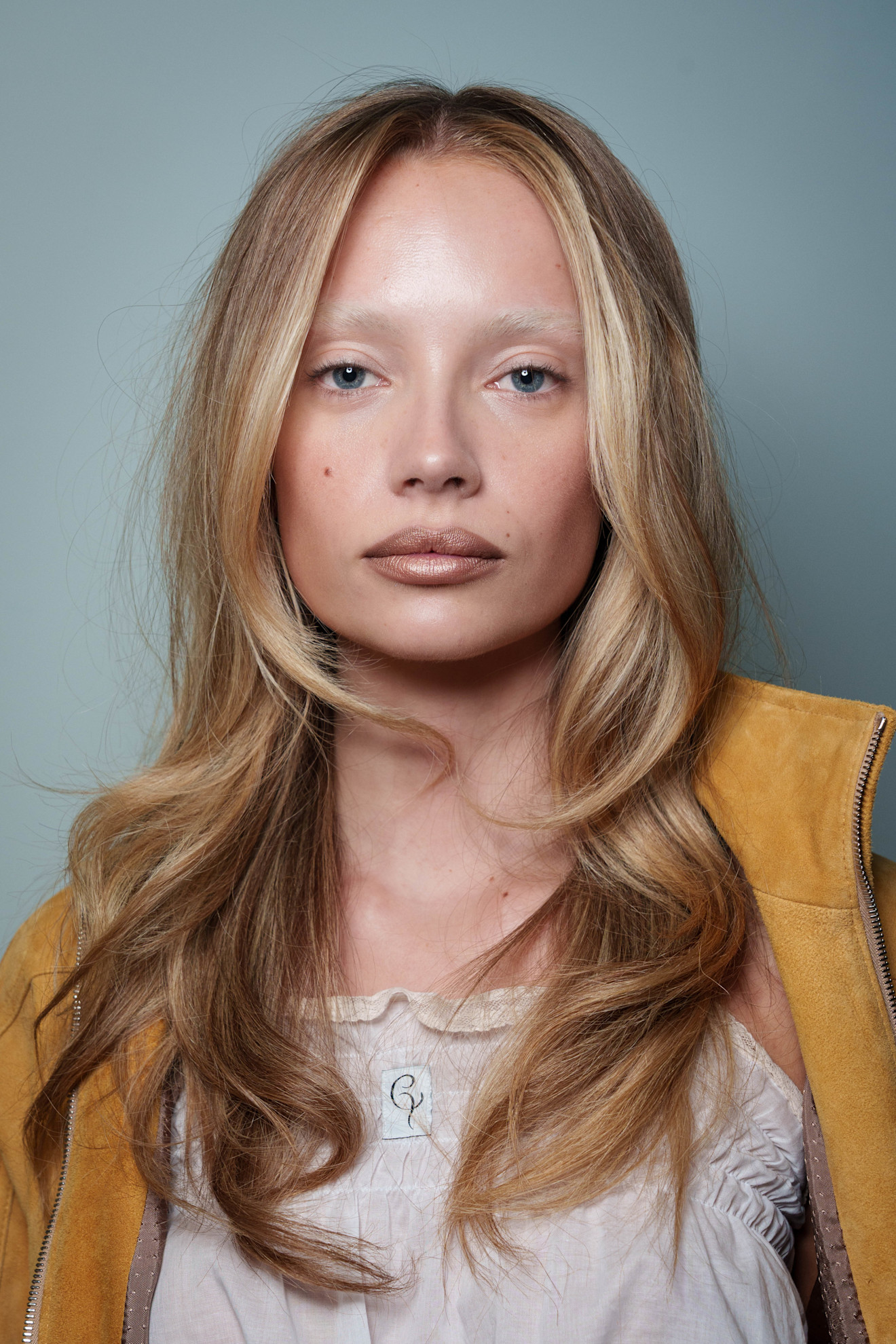A model from Conner Ives SS26 with loosely curled hair, frosted brown lipstick and bleached eyebrows