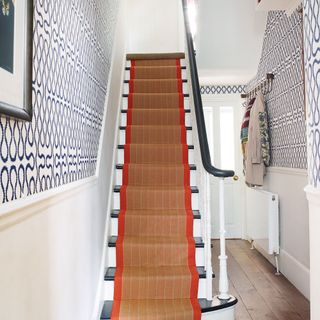 narrow hallways with wooden stairs and woven runner and patterned wallpaper