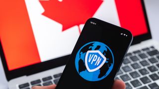Hand with mobile phone and VPN application, Canadian flag on laptop screen on the background