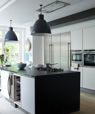 Modern kitchen ideas with a black kitchen island in a white room, with dark gray pendant lights.