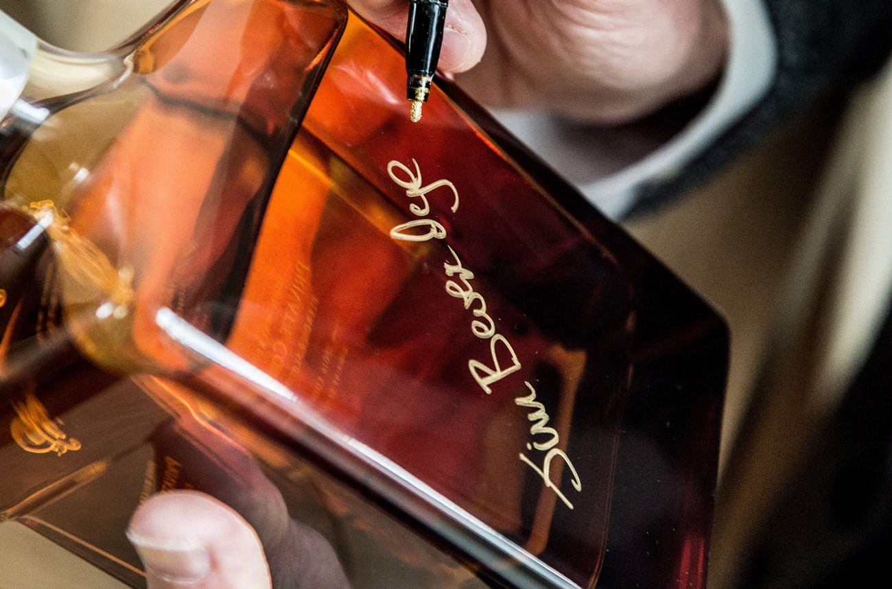 Man writing a gold signture on a bottle of whisky