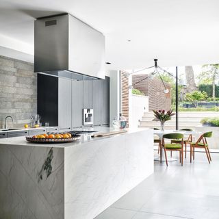 Kitchen with grey tiled concrete floor, large marbled kitchen island, floor to ceiling glass doors to the patio and garden