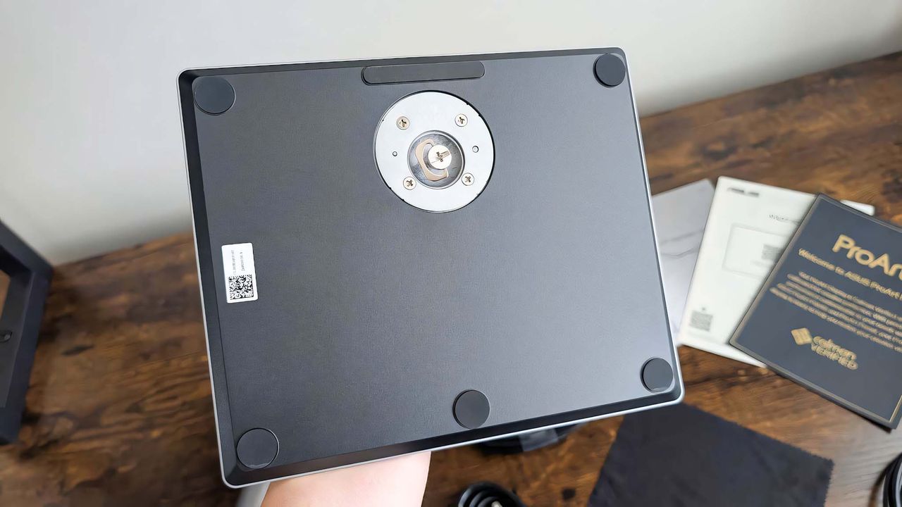 A hand holding the ASUS ProArt PA27JCV's base upside down to expose the built-in screw on the bottom.