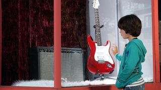 Kid looking in guitar store window at a Fender Stratocaster and Fender amp