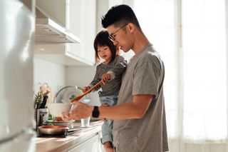 A father and young daughter cooking together in the kitchen.