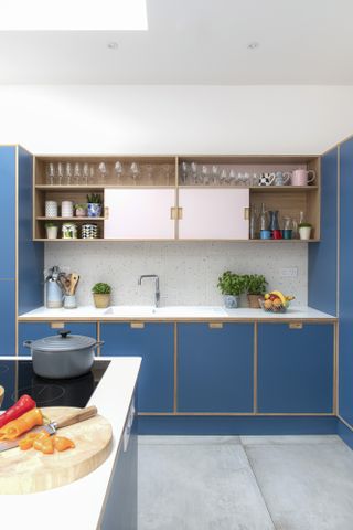 Plywood kitchen with blue and pink Formica units, oak open shelves, white worktop, terrazzo splashback tiles and grey large-format floor tiles