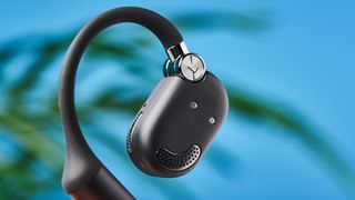 a pair of black open-ear headphones with a spring magnetic charging case photographed against a blue background