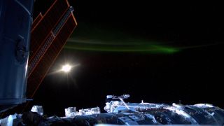 A photo of the international space station, with the moon and a faint green aurora in the background