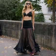 Woman wears black lace bra and long flowying sheer skirt and deep red velvet heels. 