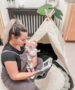 woman holding baby on a floor mat outside a teepee in a living room
