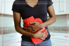 A woman holding a red hot water bottle to her tummy to illustrate one of 12 doctor recommended period pain remedies