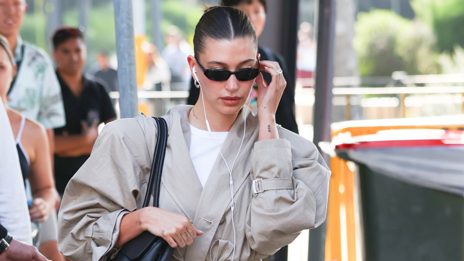 Hailey Bieber wearing a tan jacket, white pants, and kitten-heel pumps at the airport in Australia.