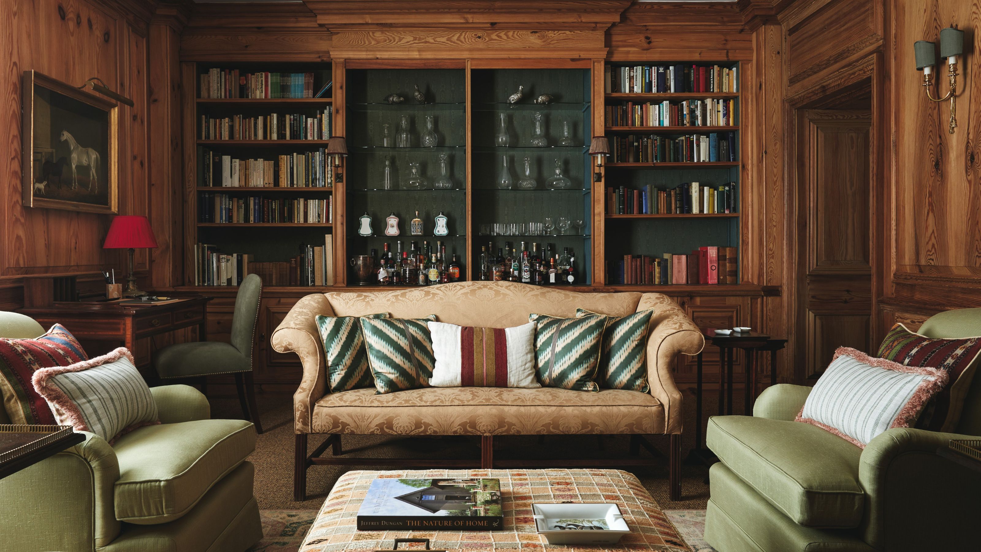 a large wood clad library with traditional bookcase, a formal settee, two green armchairs, and an ottoman