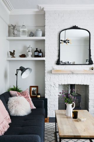A white living room with painted exposed brick, dark grey sofa and large mirror over fireplace