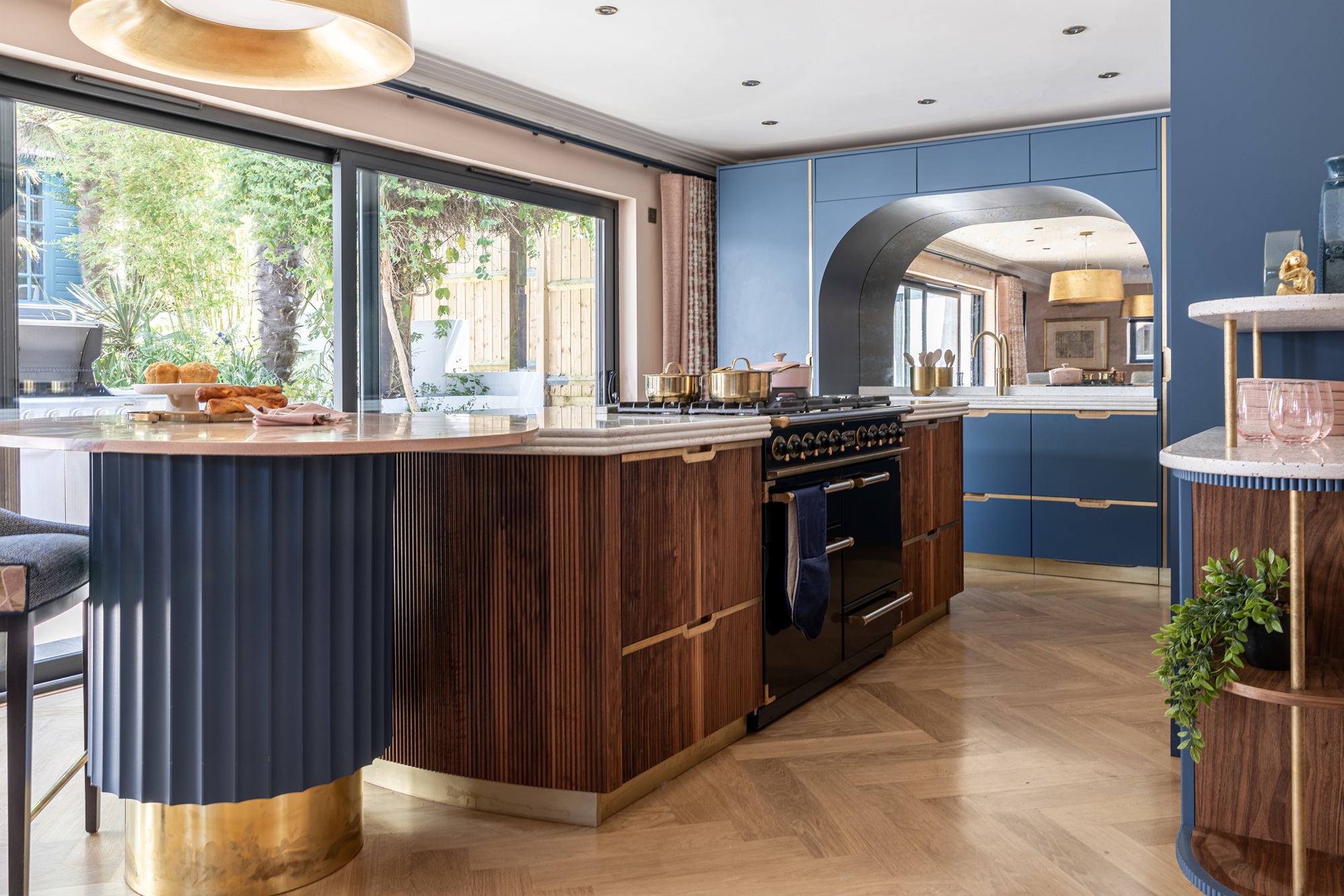 a modern art deco inspired kitchen with a wood, gold and blue color palette, with an arched ranger cooker hood and fluted island design