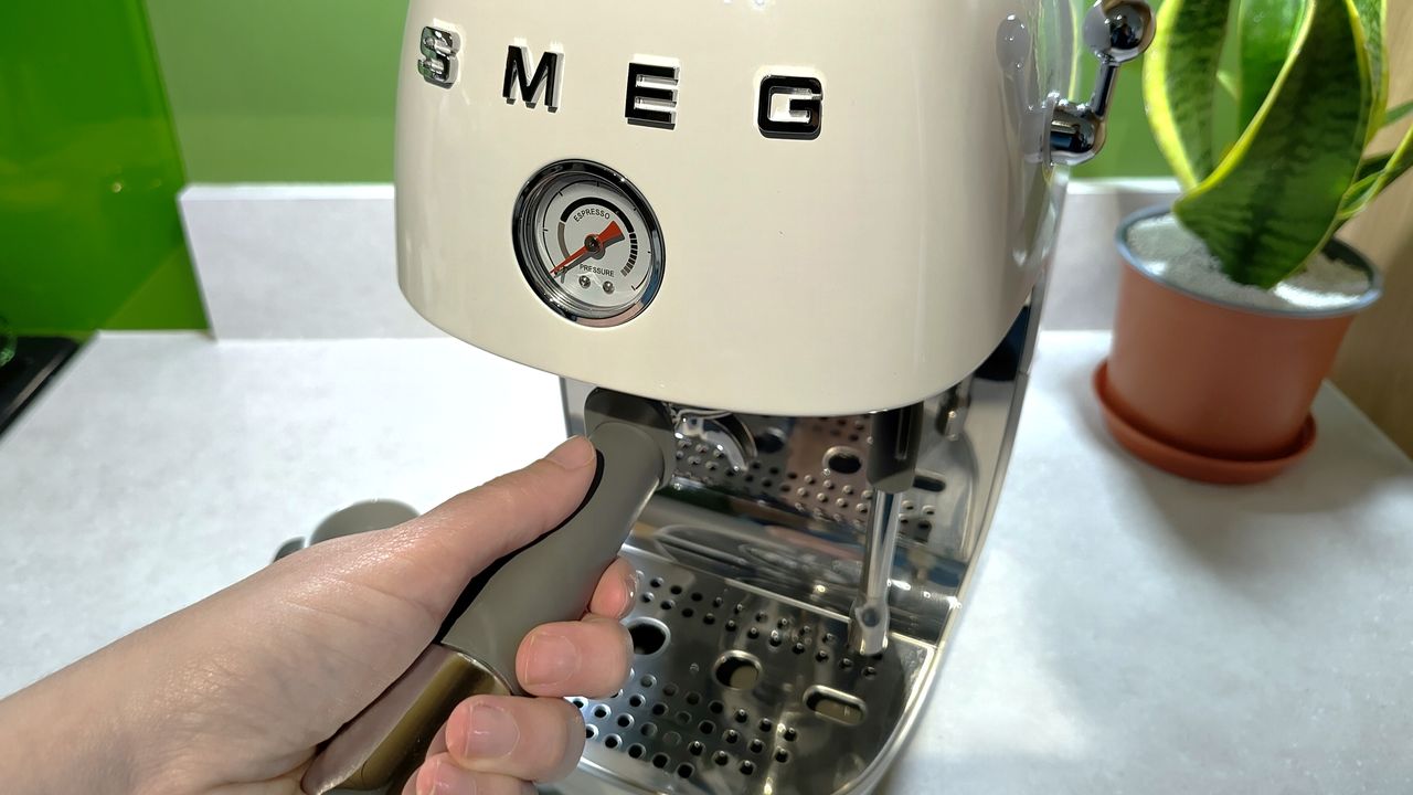 Person inserting portafilter handle into Smeg ECF03 espresso machine