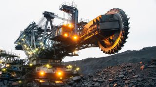 A giant bucketwheel excavator on top of a pile of broken rocks with headlights on