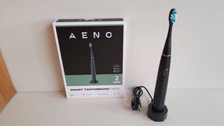 Aeno electric toothbrush sitting on wireless charging platform next to product box