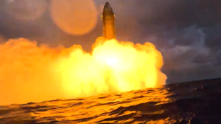 A big rocket fires its engines above the water.