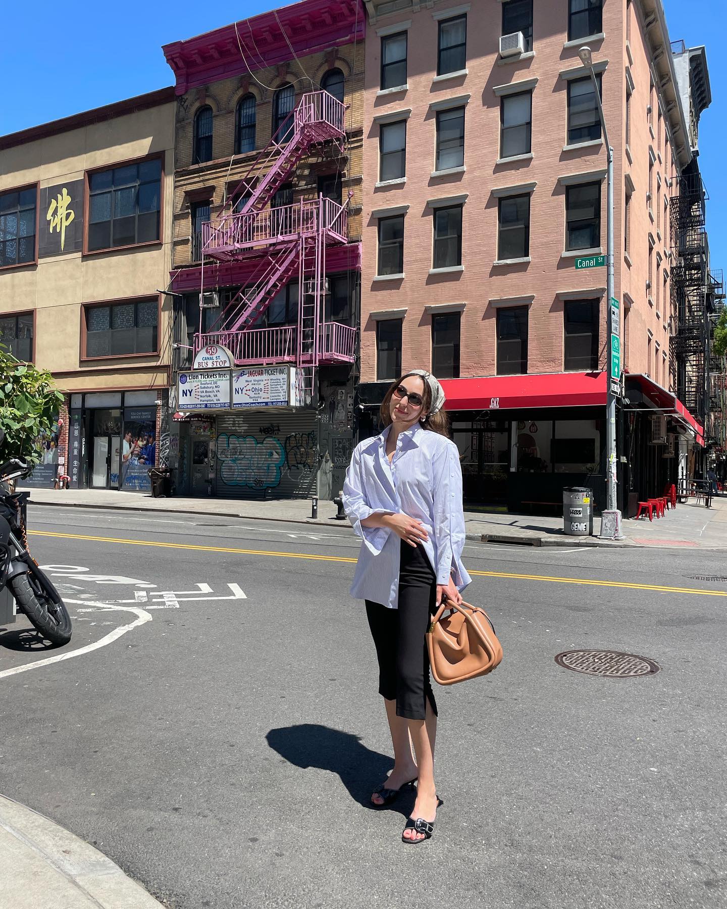 Anna LaPlaca wearing a silk headscarf with a button-down shirt, capri pants, a brown bag, and kitten-heel sandals.