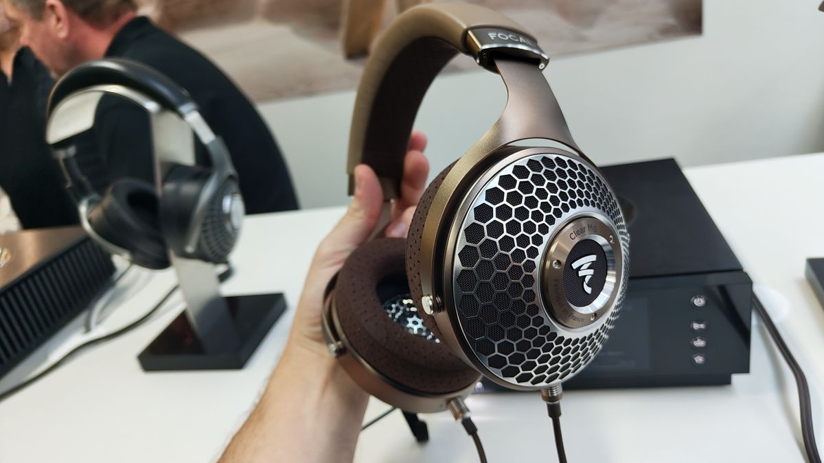 The Focal Clear Mg headphones held in the hand in front of a hi-fi component and another pair of headphones on a headphone stand.