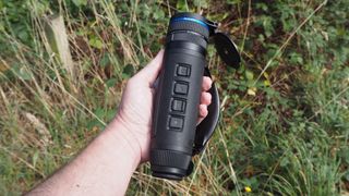 Pulsar Telos XQ35 monocular held in a hand outside in front of a green bush