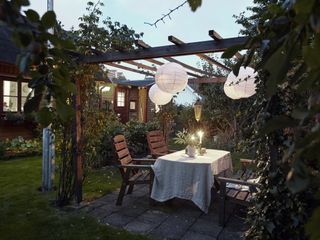 a pergola with lanterns for relaxed boho vibe, and a simple outdoor dining set with a white tablecloth, with candles and plants on top