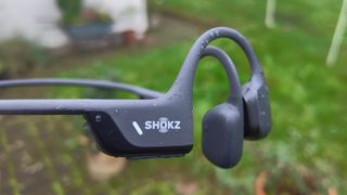 Shokz OpenRun Pro 2 in-ear headphones held above garden lawn