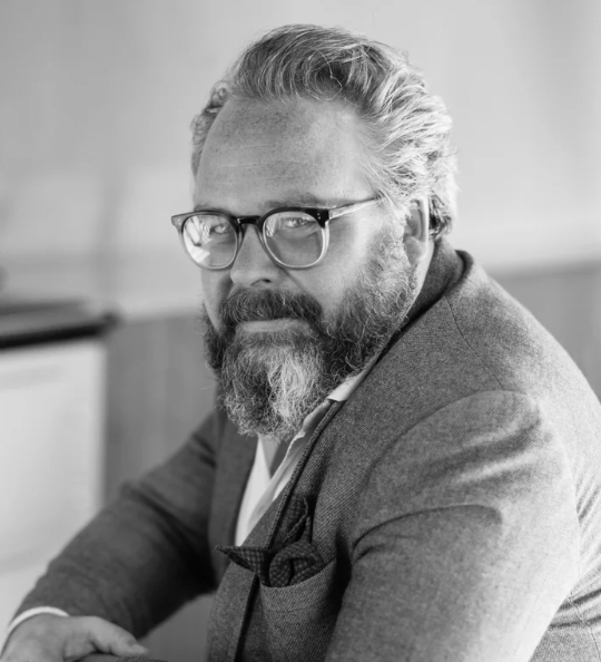 A grayscale headshot of a man wearing glasses 