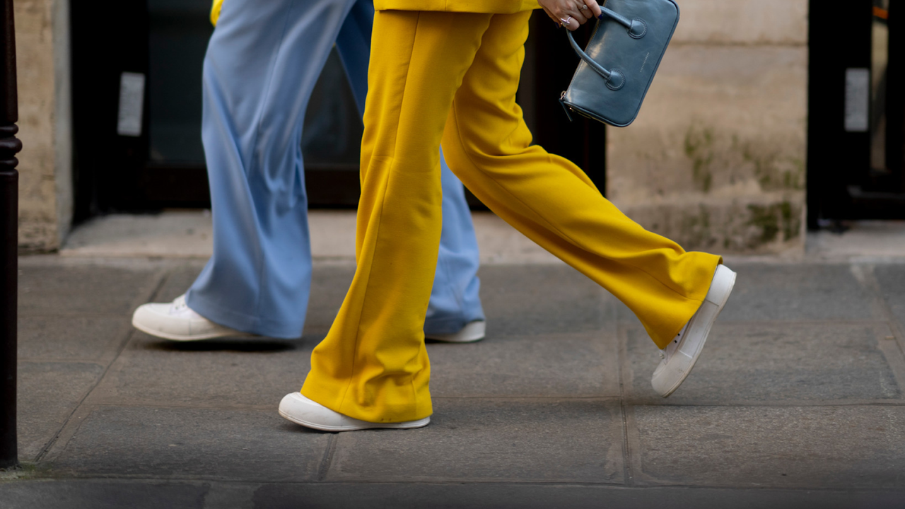 two people walking wearing blue and yellow pants, white sneakers, and a blue handbag