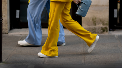 two people walking wearing blue and yellow pants, white sneakers, and a blue handbag