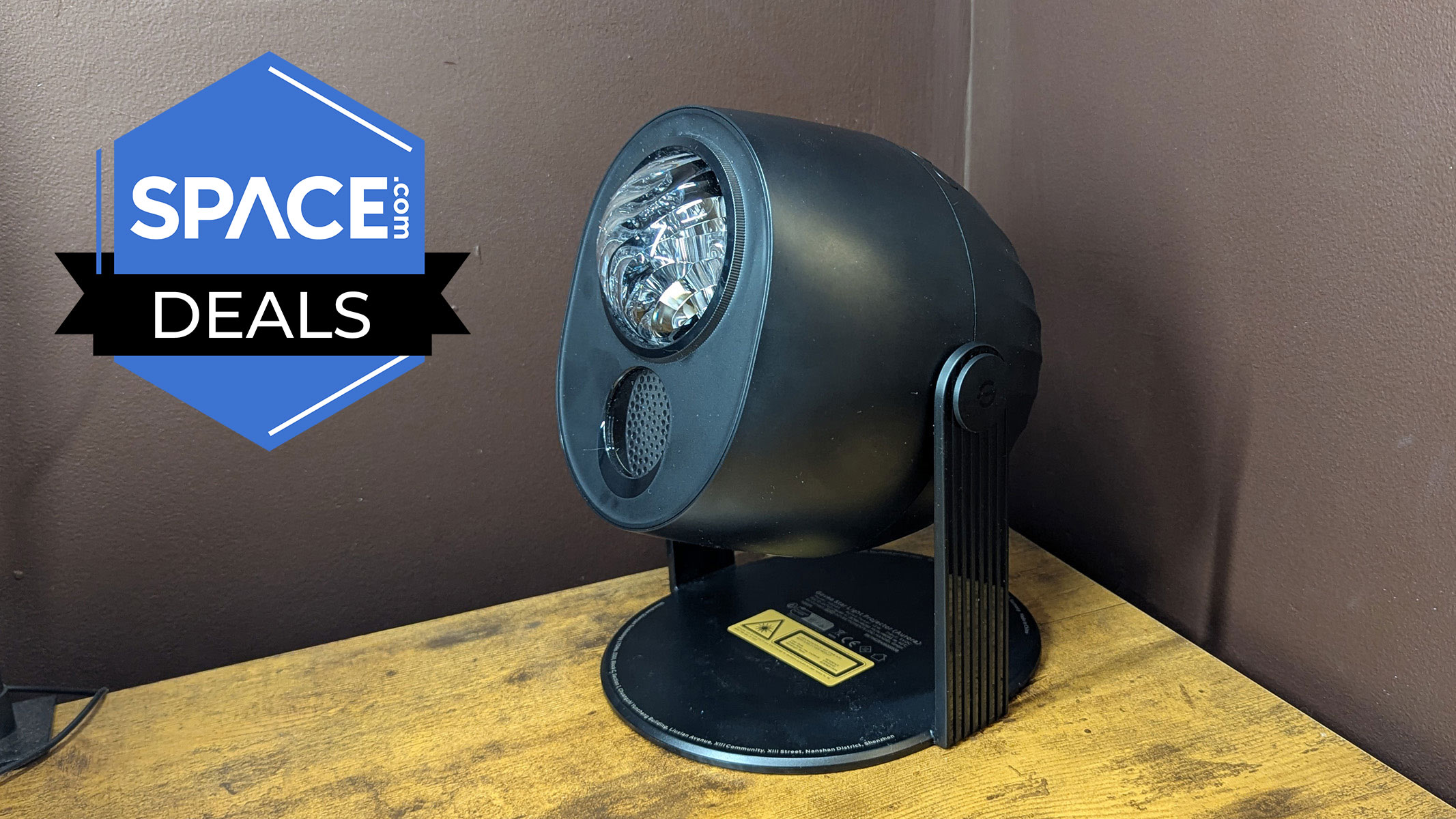 A projector sits on a brown wooden surface with a marron-colored wall behind it and the space.com logo in the top left corner.