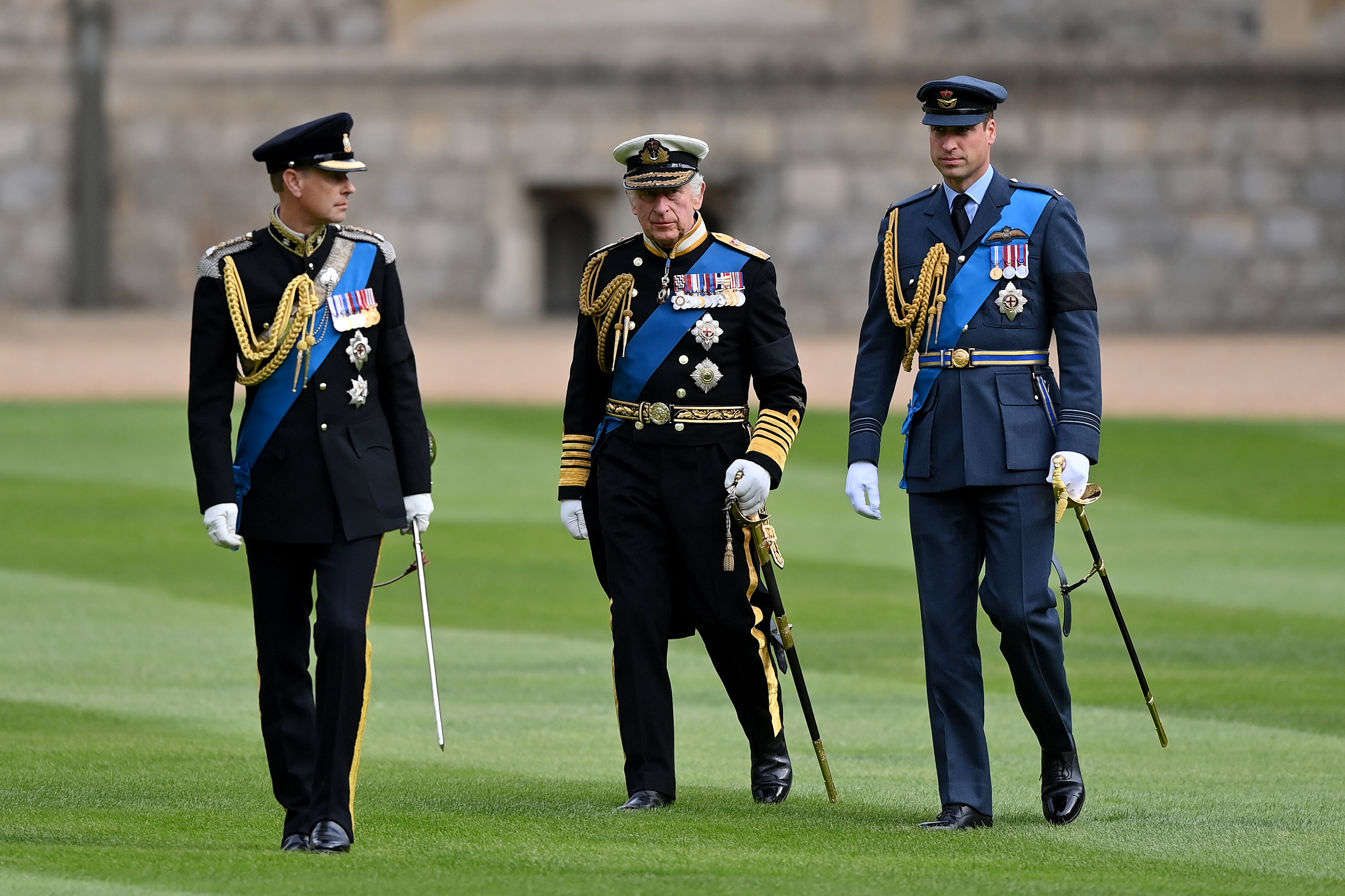 Prince Edward, King Charles and Prince William wearing uniforms walking on grass