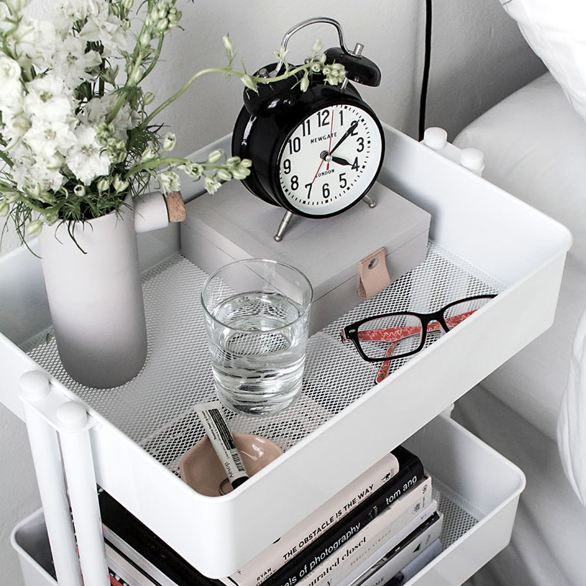 Troli putih digunakan sebagai meja samping tempat tidur yang memajang kebutuhan sehari-hari