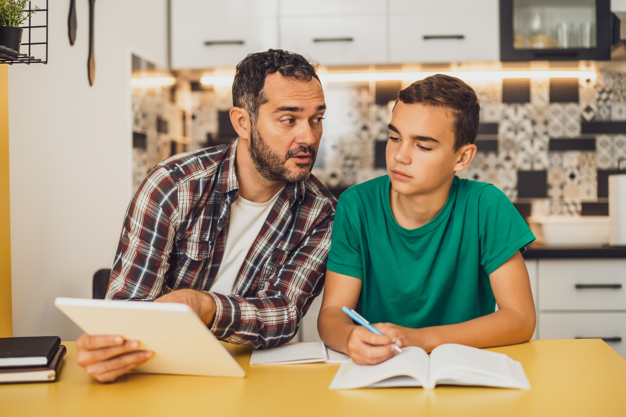 Father is helping his son with learning. They are doing homework together.