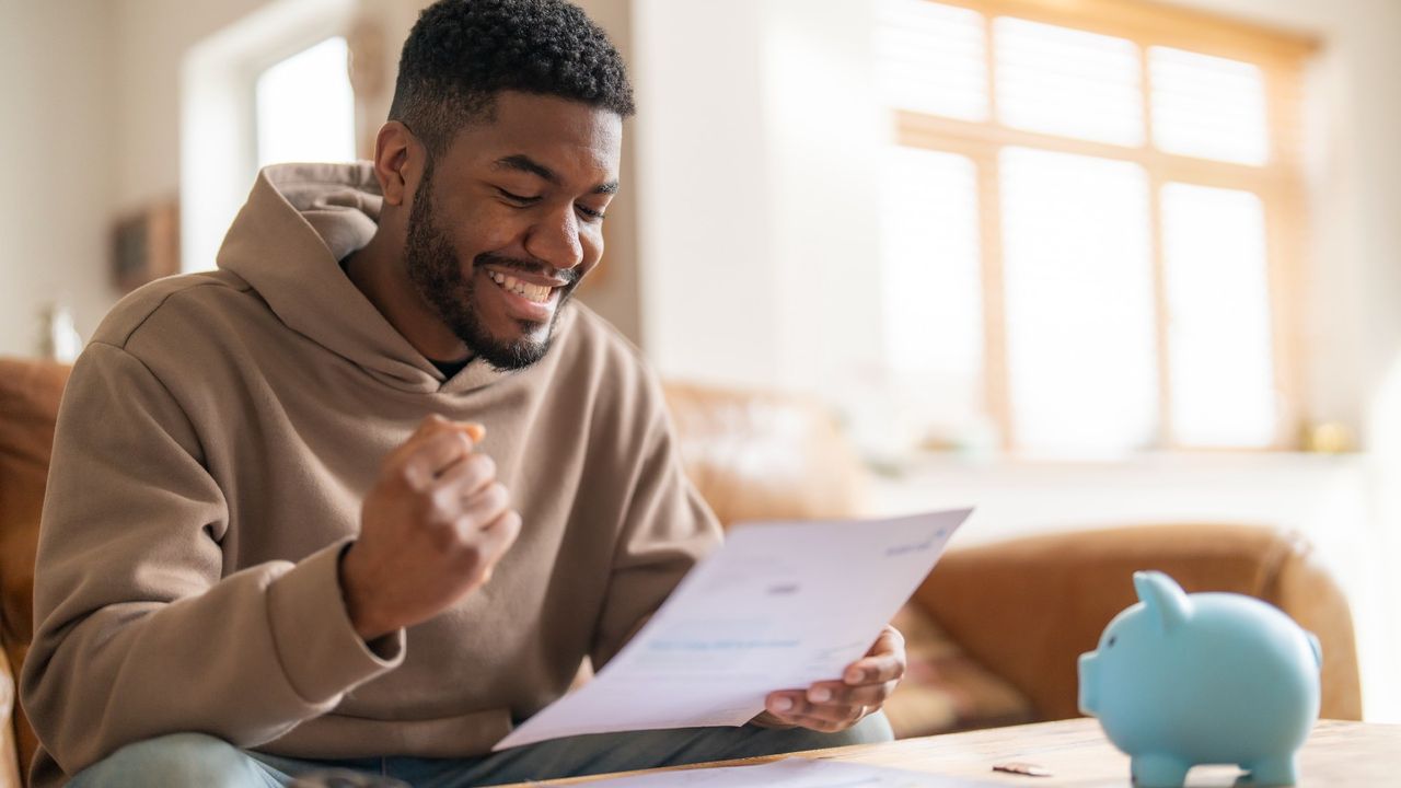 Happy-looking man reading through financial documents next to a piggy bank