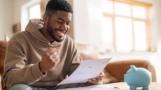 Happy-looking man reading through financial documents next to a piggy bank