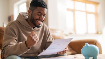 Happy-looking man reading through financial documents next to a piggy bank