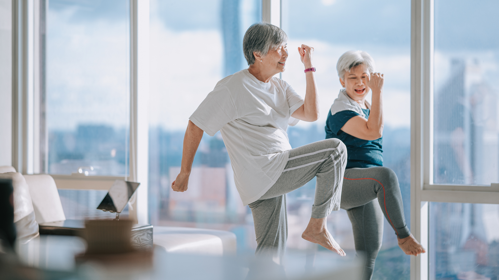 Two women in a domestic setting exercising, with one knee raised in the air.
